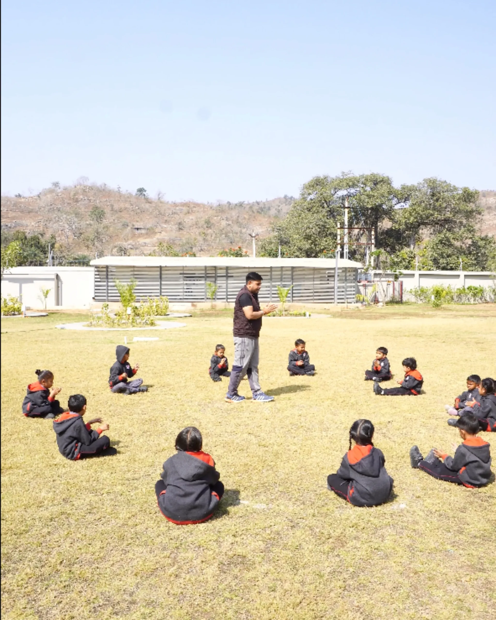 Children Sitting In Circle With Teacher Outdoors