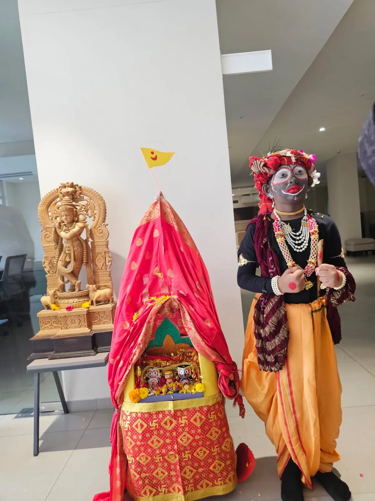 A close-up view of three brightly painted wooden Hindu deities—Balabhadra, Subhadra, and Jagannath—resting inside a decorated shrine with pink and yellow flowers, displayed at Shree Shakti School of Innovation (SSI)